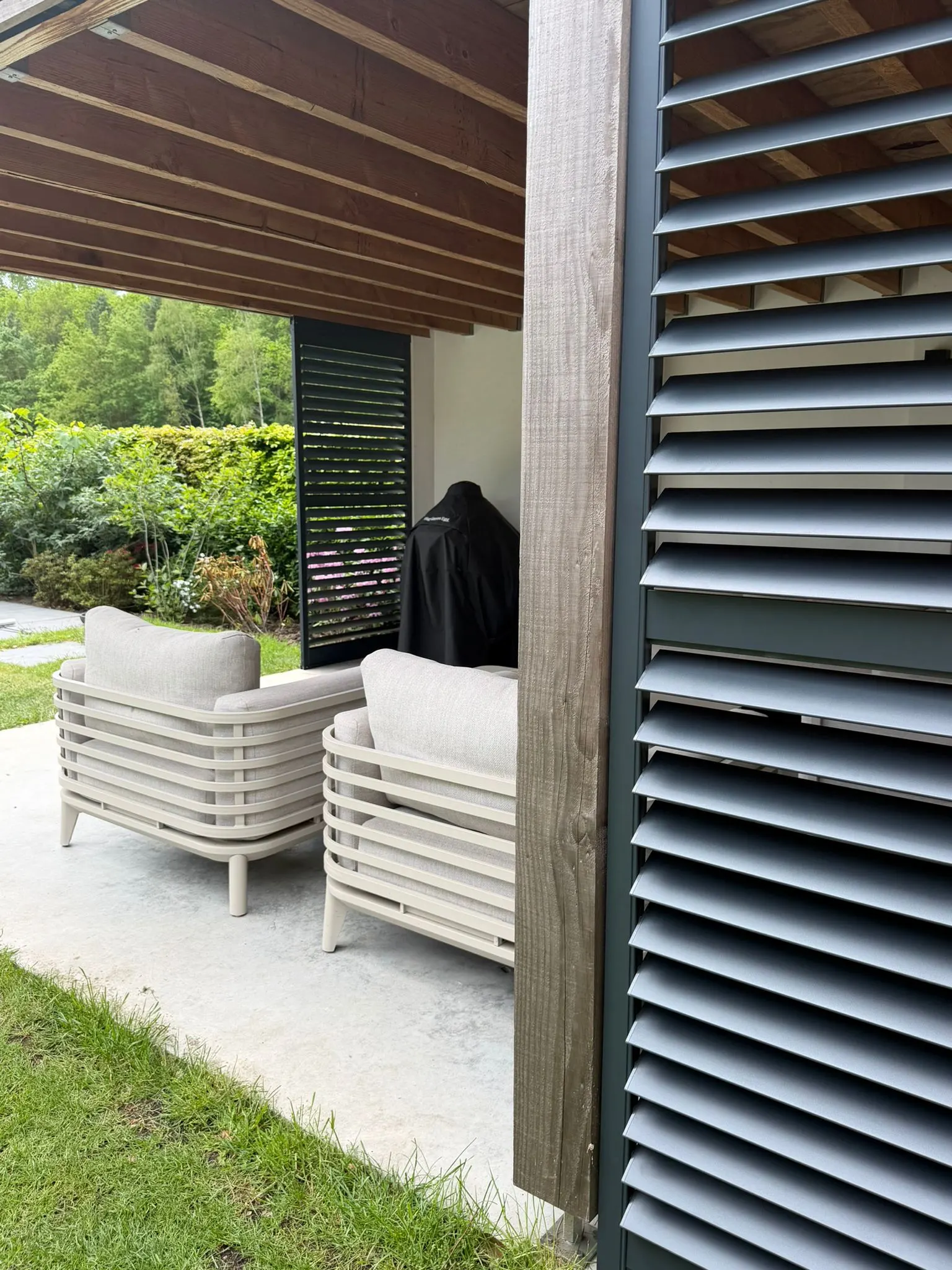 Dark aluminium outdoor shutters with mid-rail on a modern home patio